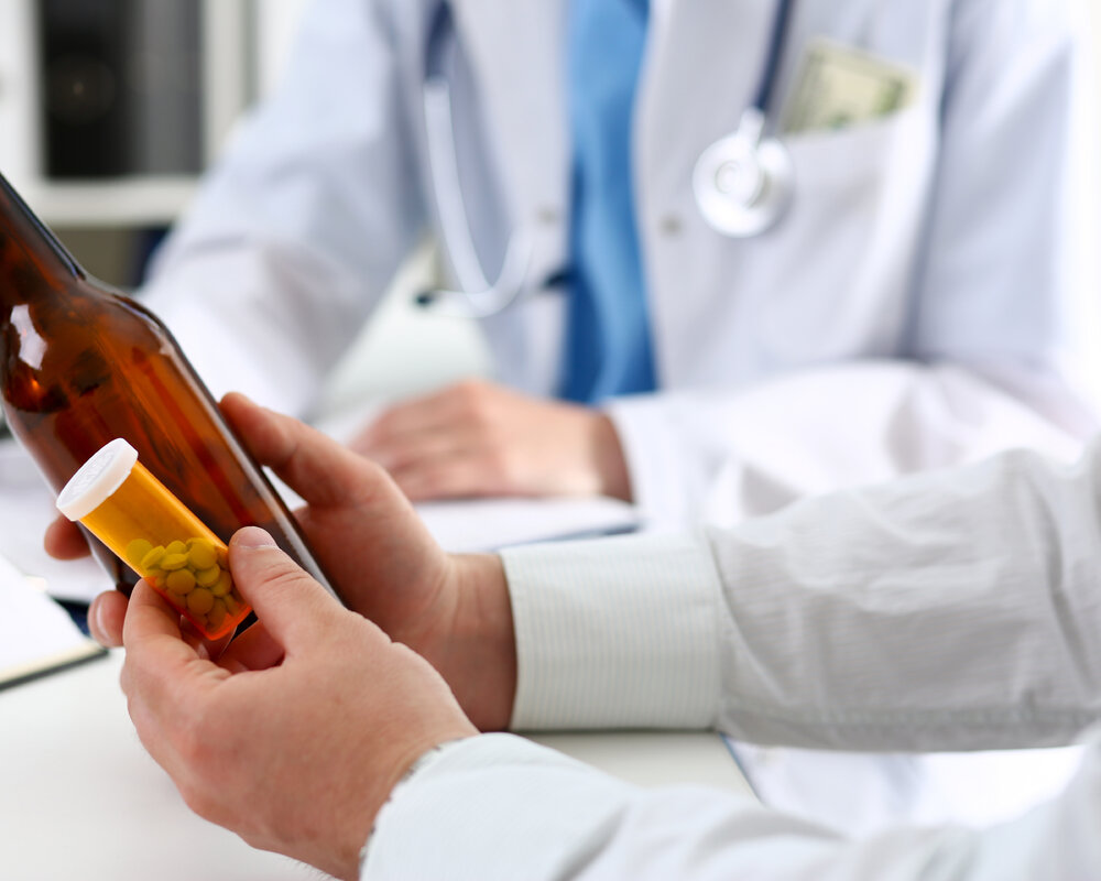 алкоголик держит бутылку и таблетки на приеме у врача