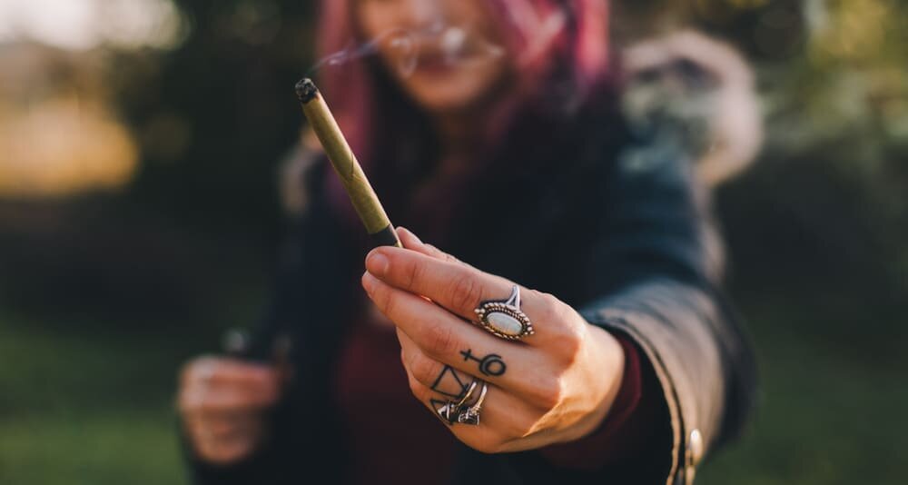 Девушка протягивает сигарету с марихуаной